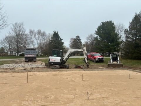 Construction site with excavators and a red pickup beside a dirt lot under overcast skies