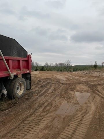 Red dump truck on muddy construction site under cloudy sky