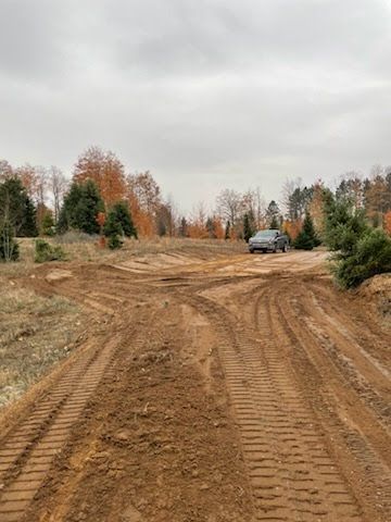 Rutted dirt road through an autumn forest under a cloudy sky, with a car in the distance