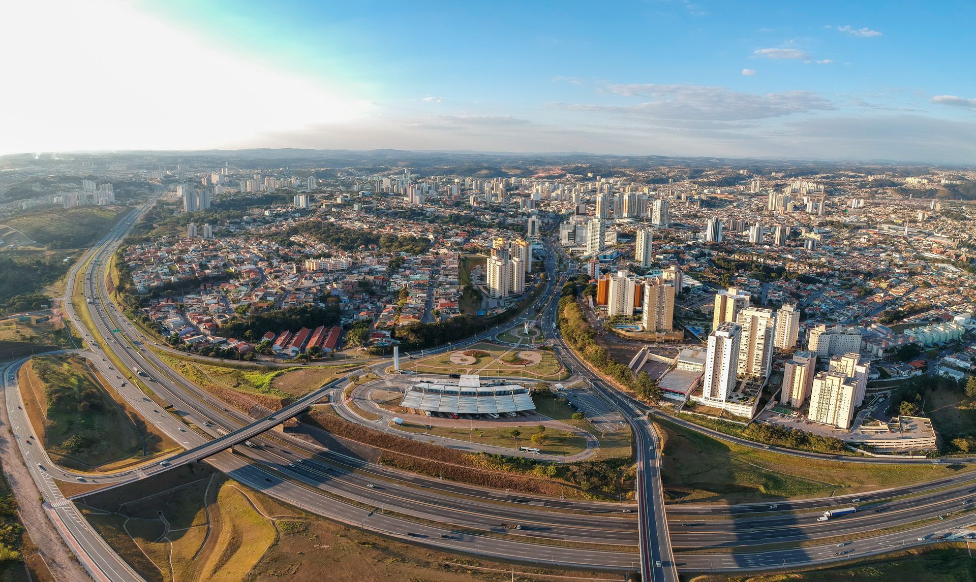 Vista aérea de uma cidade densa com rodovias, prédios residenciais e um amplo horizonte urbano sob um céu limpo.