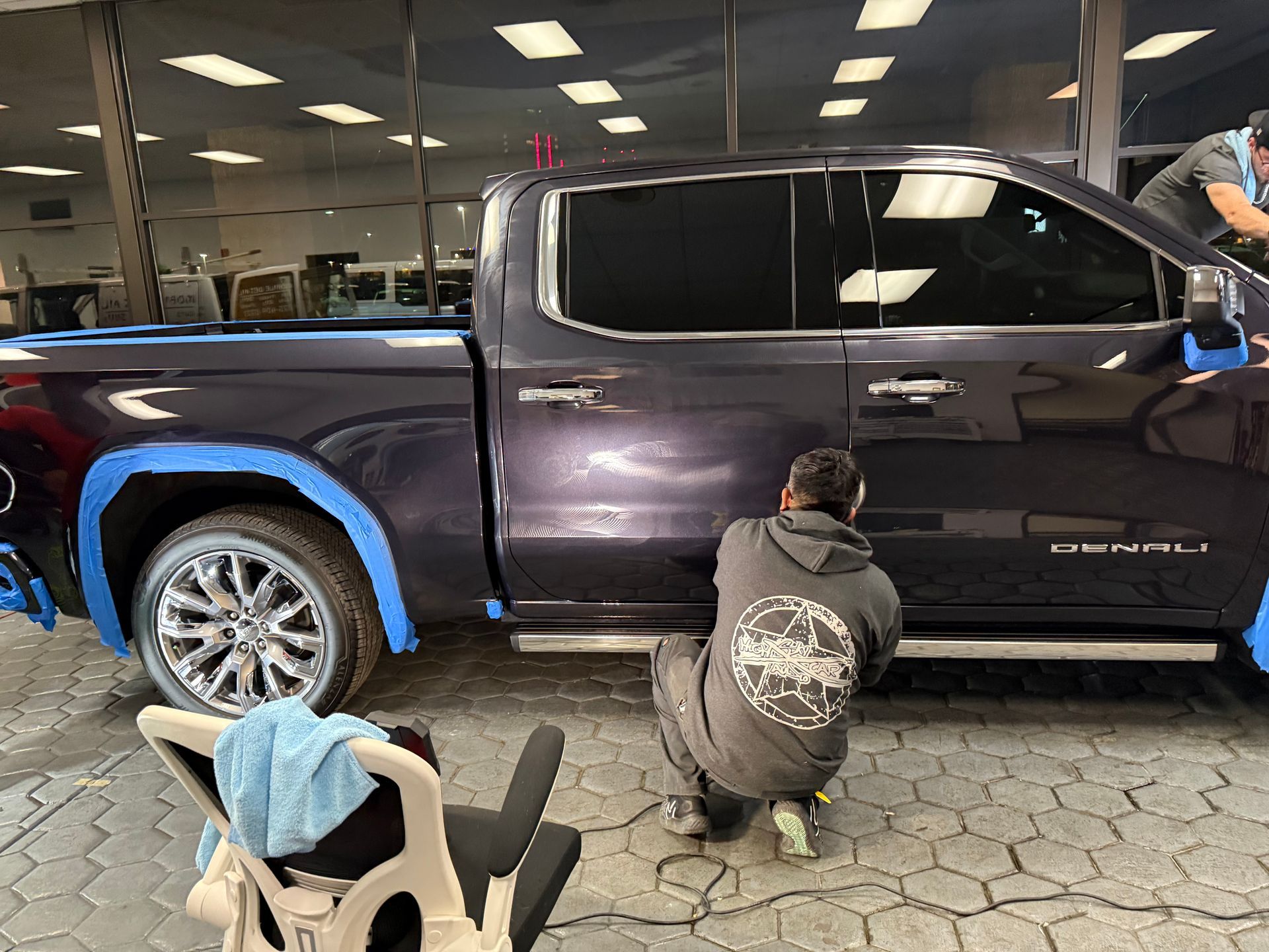 A man is kneeling down next to a truck in a garage.