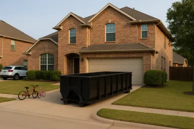 A black dumpster sits in front of a two-story brick house with a garage. Two bikes sit to the left.