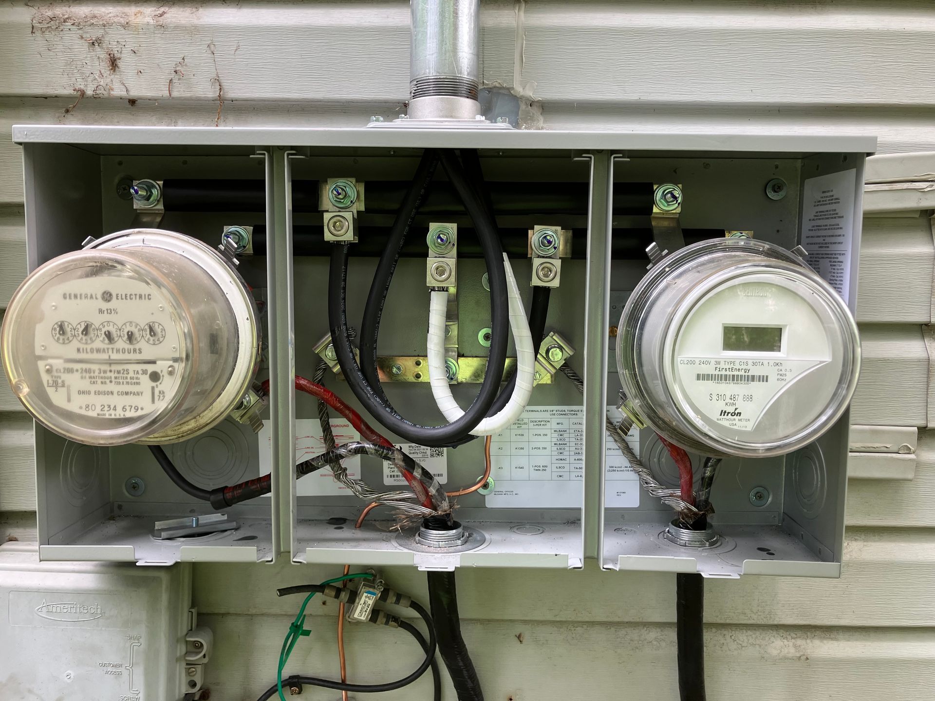 Three utility meters with wiring in an open outdoor meter box on a house wall