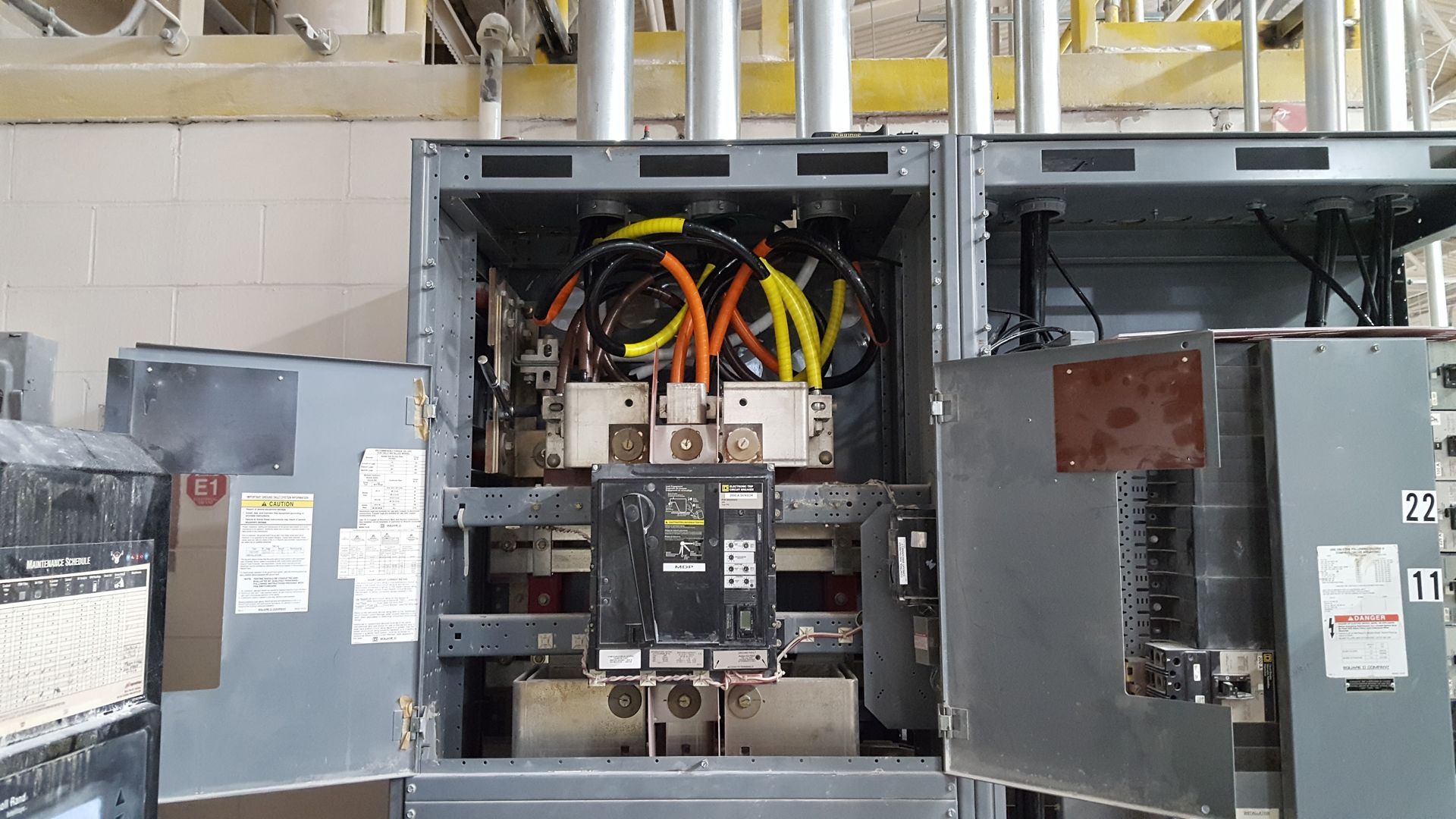 Open electrical switchgear cabinet with exposed wiring and circuit breakers in an industrial room