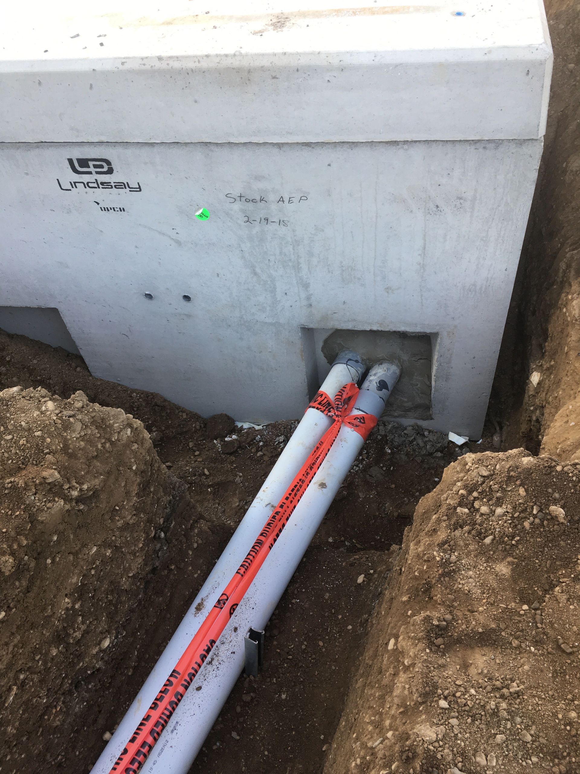 White utility box with a green light and two red-striped pipes entering through a trench in the ground