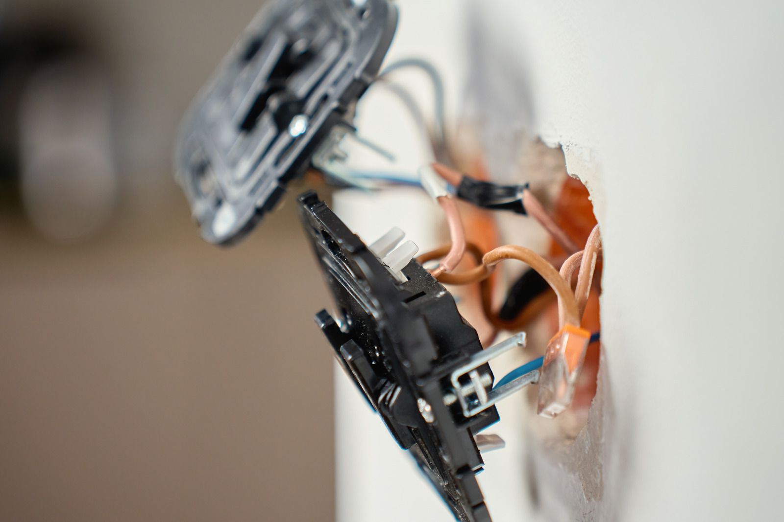 Close-up of exposed electrical wiring and a damaged wall outlet switch with orange and black wires.