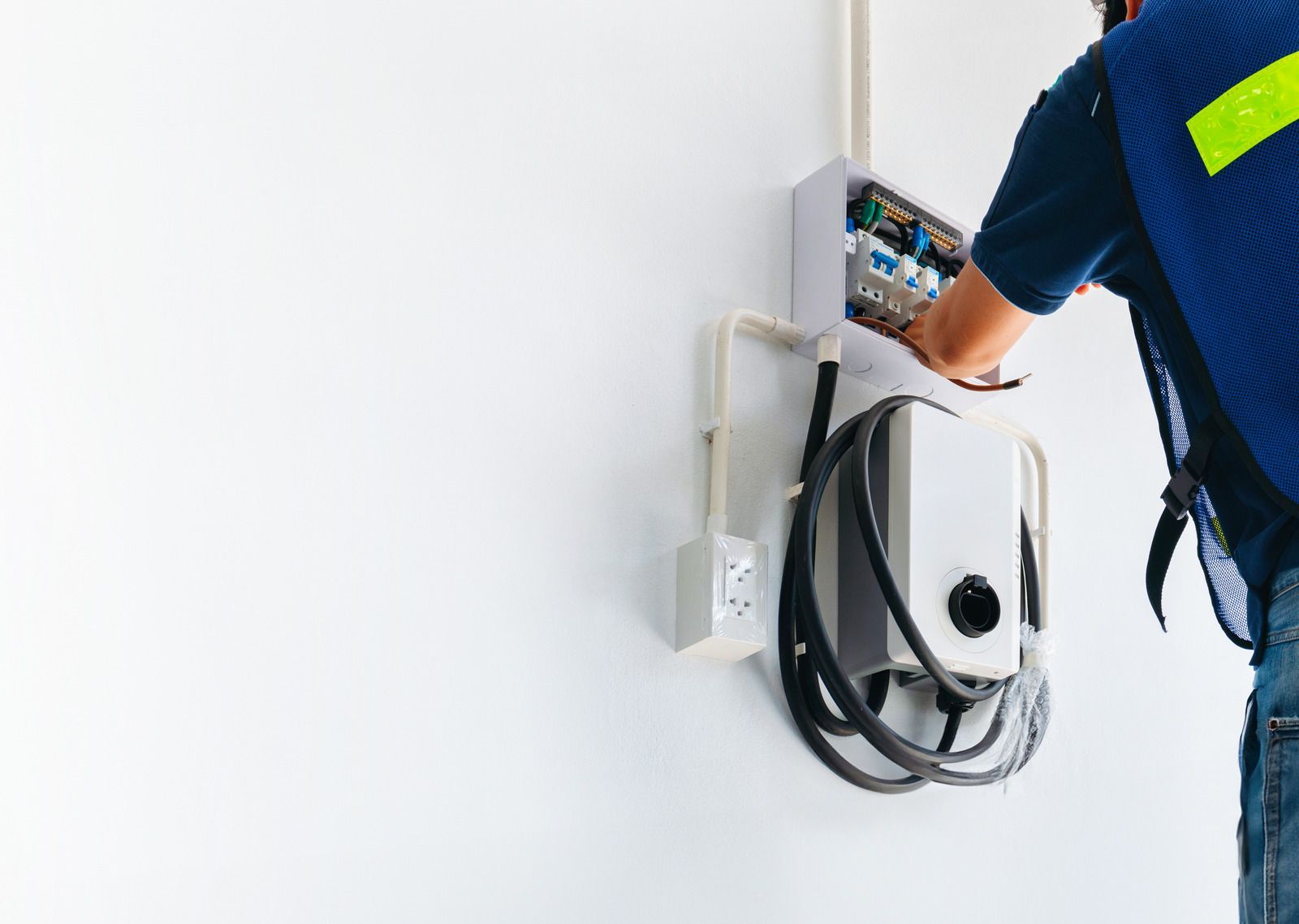 Technician installing a wall-mounted EV charger with coiled black cable and control box