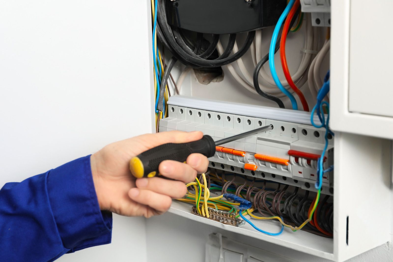 Hand using a screwdriver to wire an open electrical breaker panel with colored cables