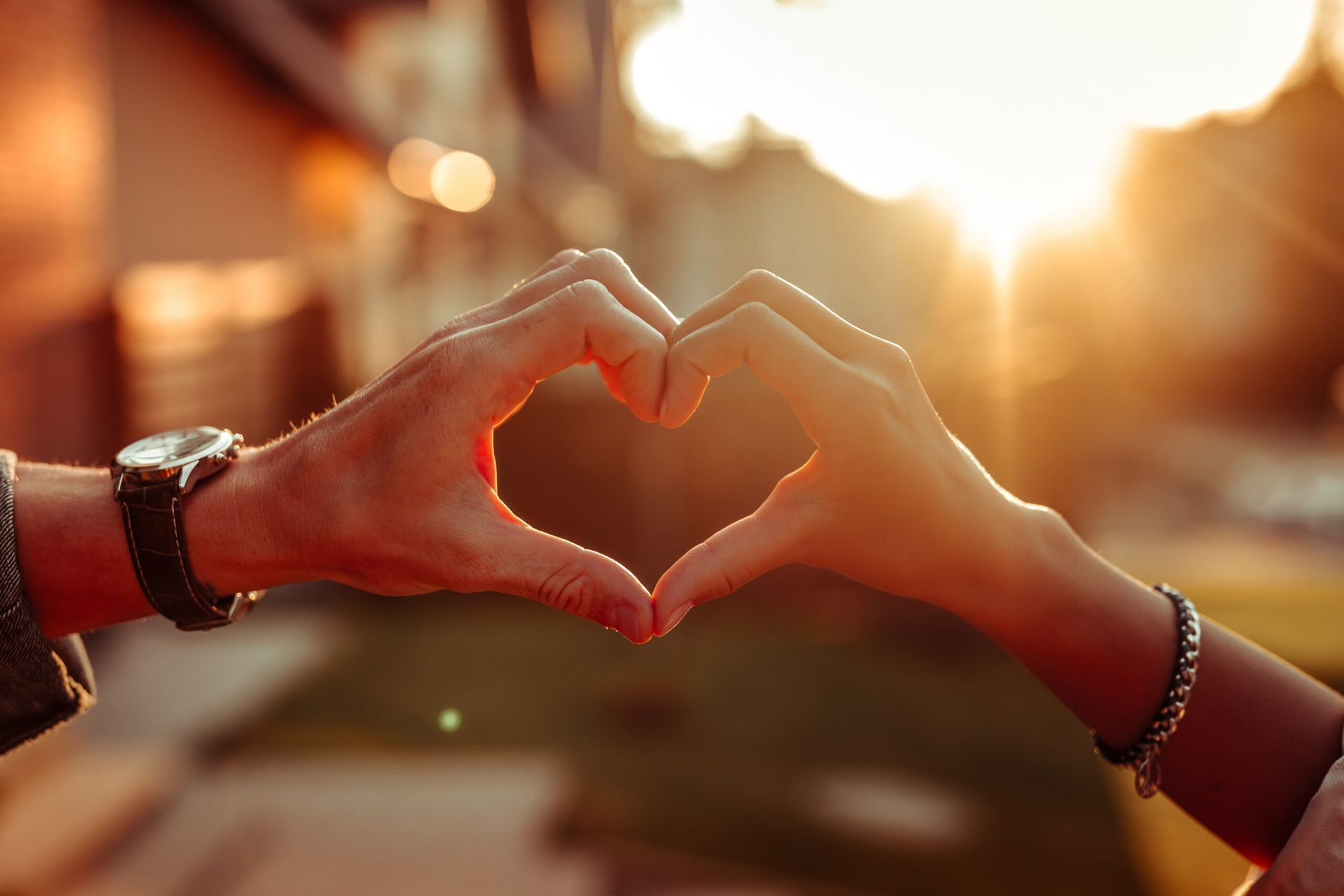 Two hands forming a heart shape against a warm sunset sky
