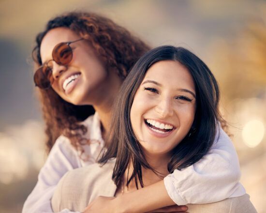 Two smiling friends hugging outdoors, with a blurred warm background