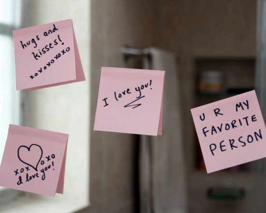 Pink sticky notes with handwritten love messages on a refrigerator door.
