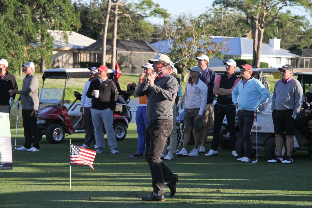 Group of golfers watching a man tee off, golf course setting, sunny day.