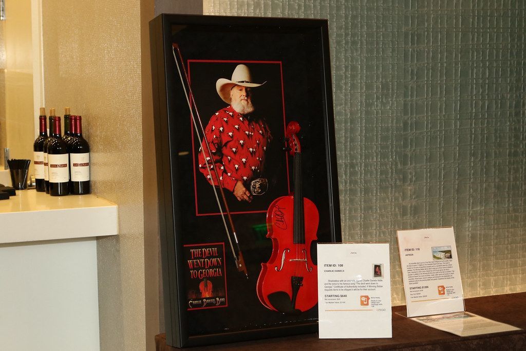 Painting of a man with a cowboy hat and red violin. Red, black, and white bottles and brochures.