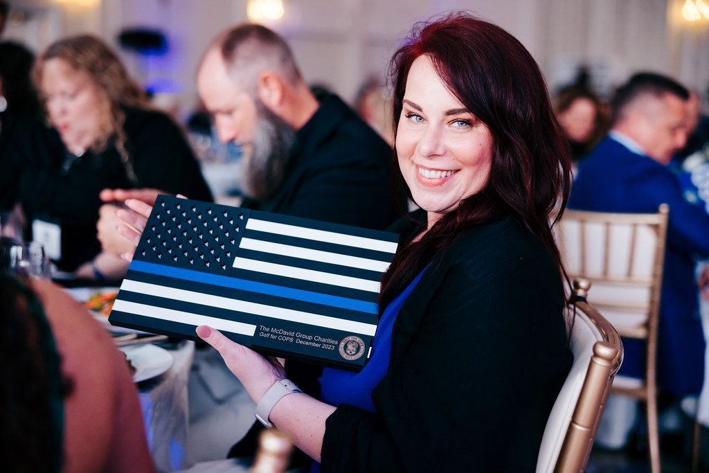 Woman smiling, holding a blue line flag award. Attending an event, seated at a table.