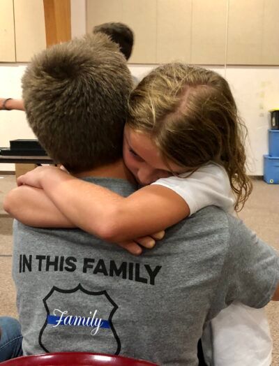 A child hugs a person wearing a shirt that says