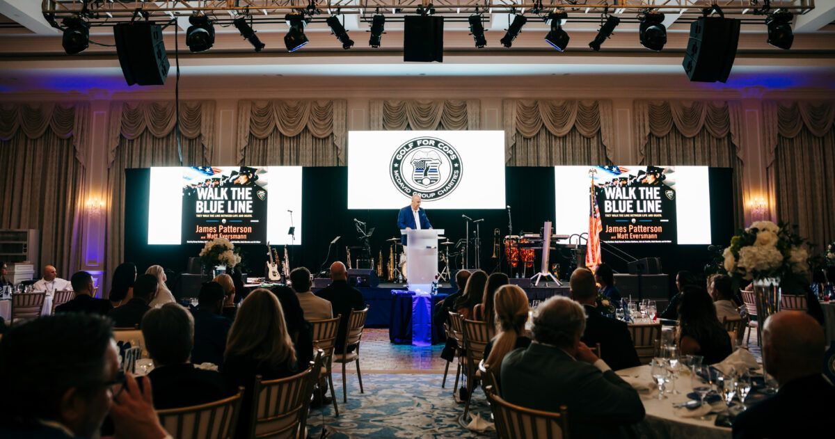 Man speaking at podium onstage during event with audience seated at tables.