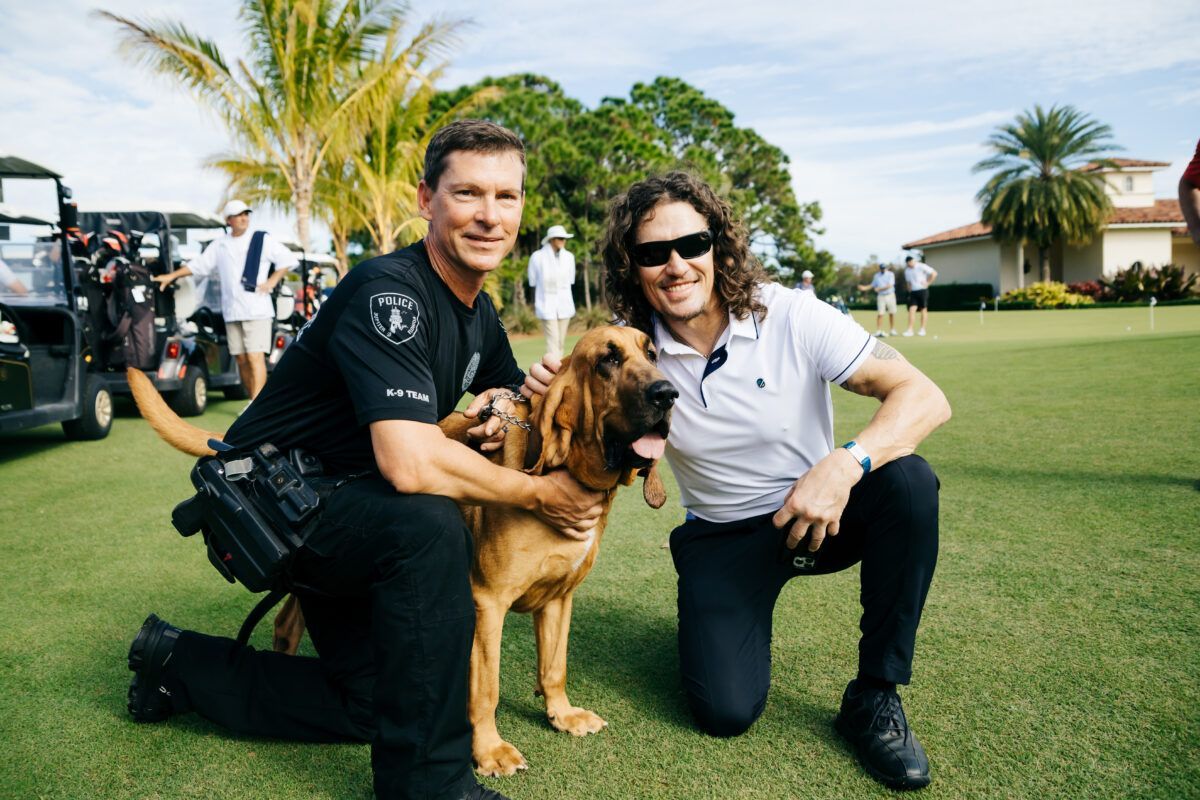 Man in uniform and man kneeling with a Bloodhound on a golf course.