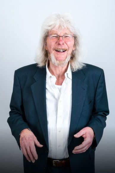 Ein Mann mit langen Haaren und Brille trägt eine blaue Jacke
