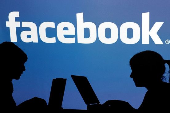 Silhouettes of two people working on laptops in front of a blue background with the Facebook logo.