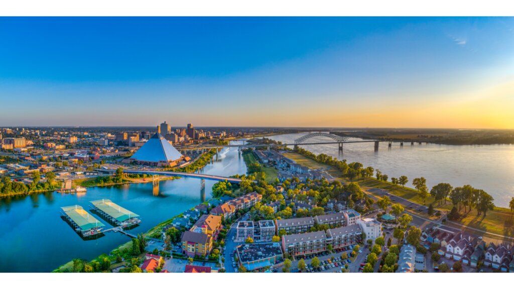 An aerial view of the Memphis skyline, including the Pyramid and Mississippi River, during a sunset.