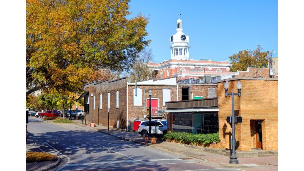 A historic downtown street with autumn trees, brick buildings, and a white clock tower under a clear blue sky.