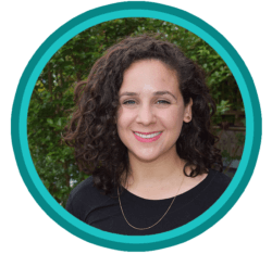 A person with dark, curly hair wearing a black shirt, smiling in front of green foliage, framed in a teal circle.