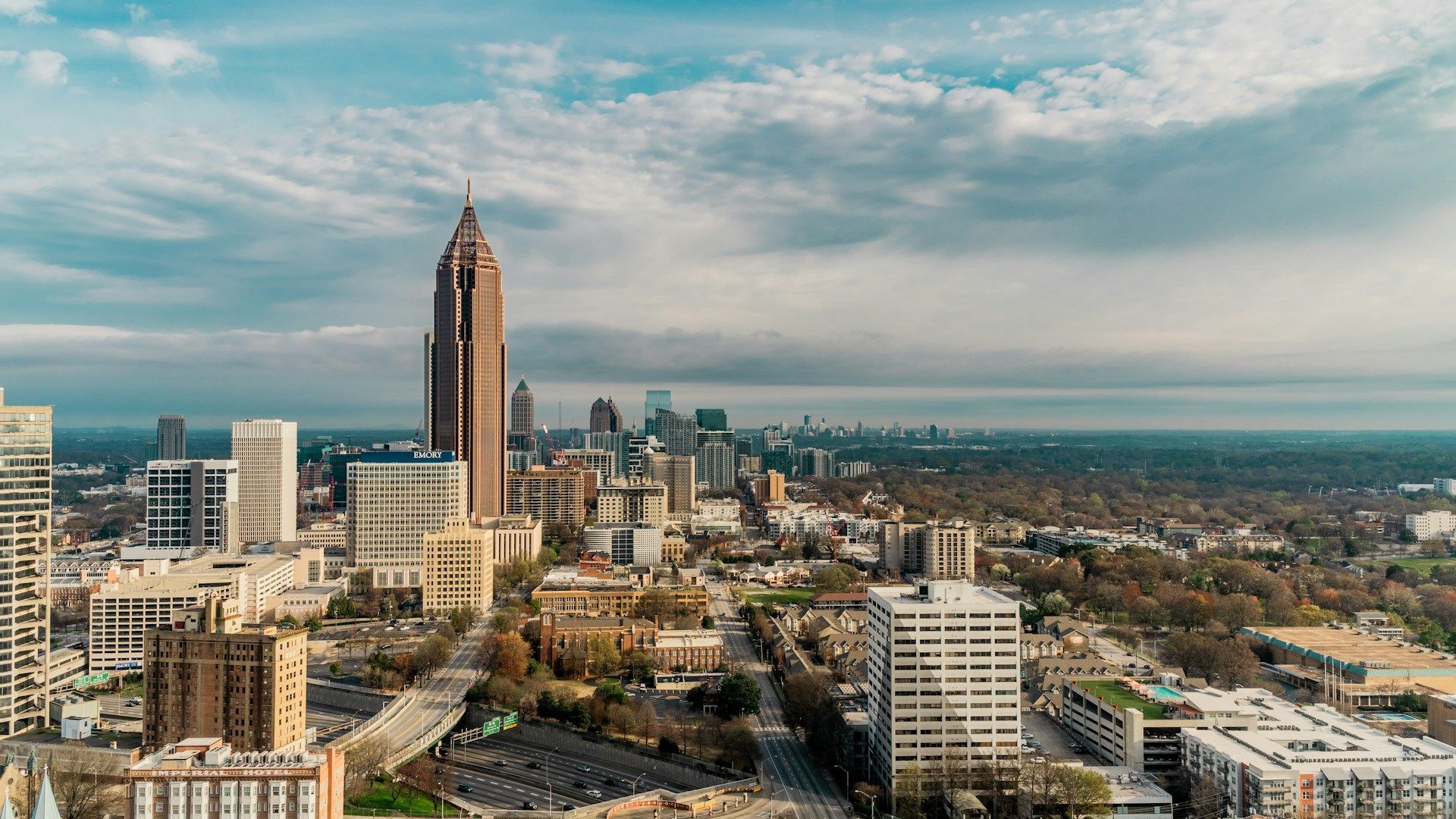 Aerial view of the Atlanta skyline at sunset, featuring the Bank of America Plaza tower under a cloudy sky.