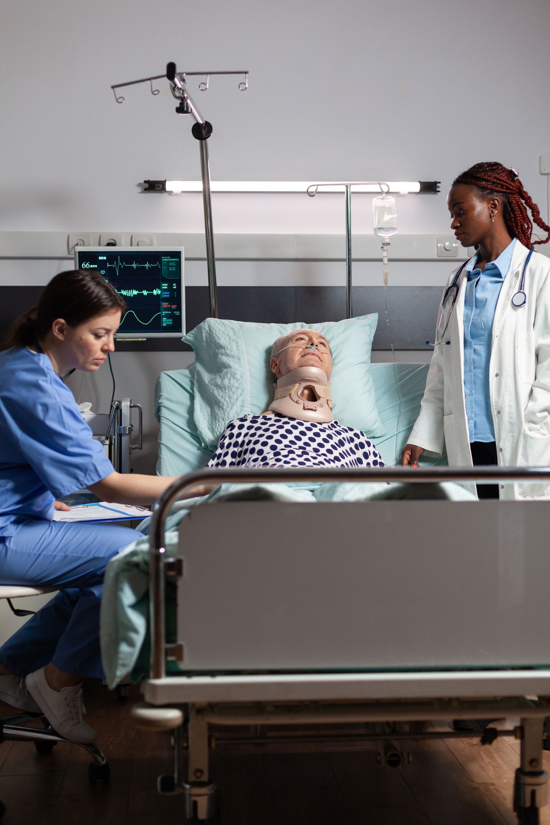 Hospital room with patient in neck brace, being attended by two medical professionals.