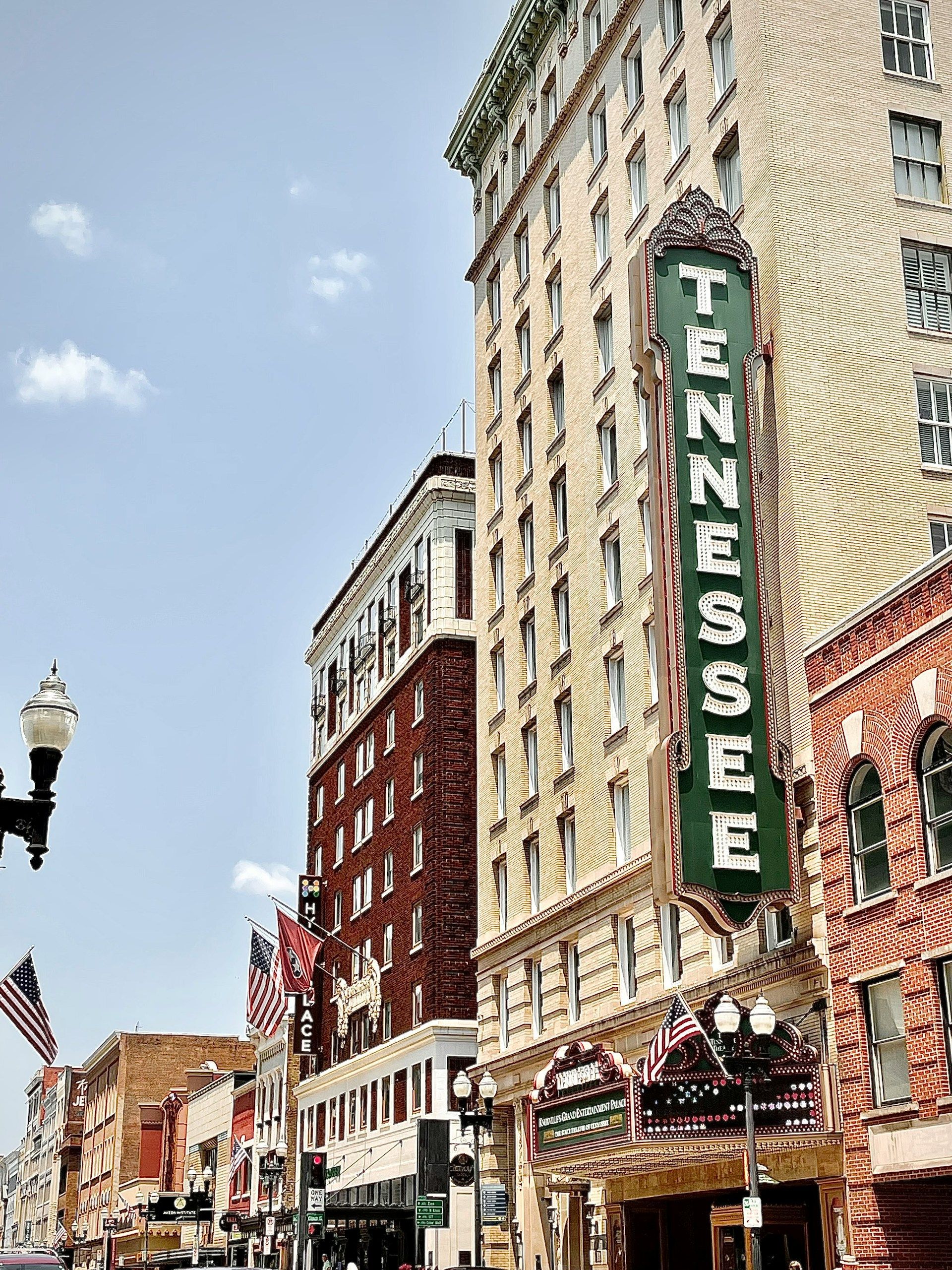 The historic Tennessee Theatre marquee on a cream-colored building, with a red brick building and American flags nearby.