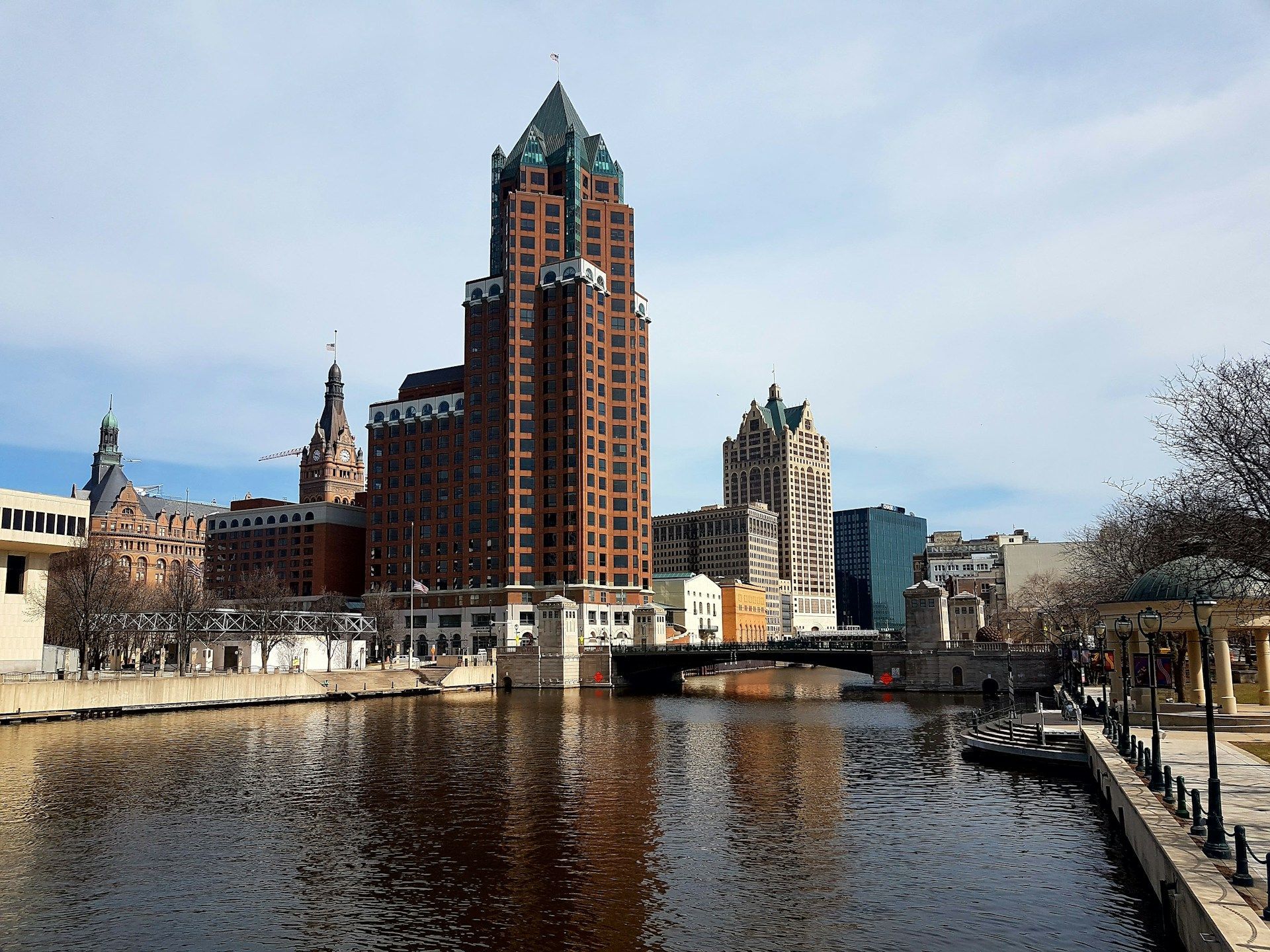 Milwaukee skyline reflecting on a river, featuring a tall brick skyscraper with a teal top.