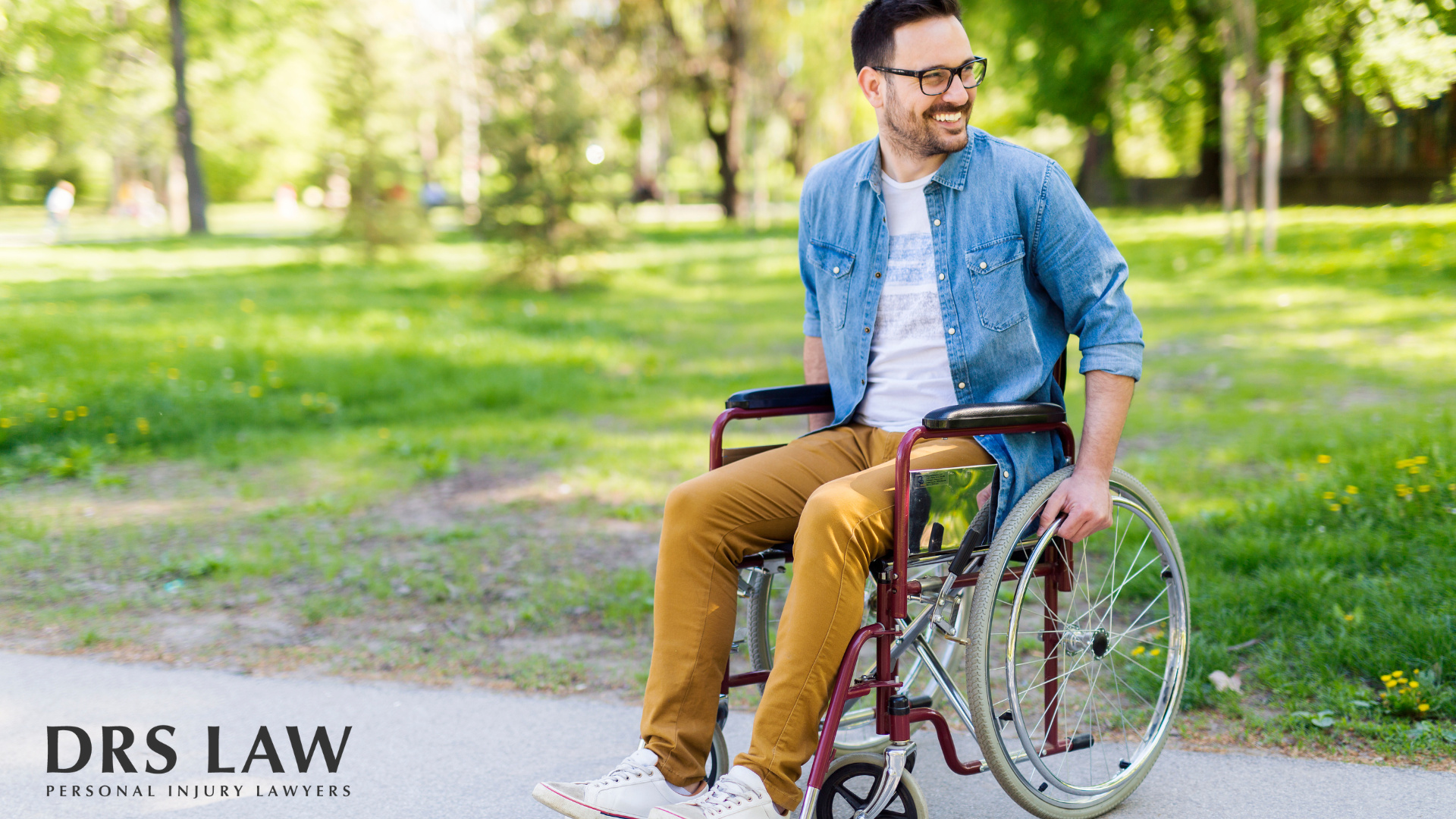 A person in a wheelchair smiles while outdoors on a paved path in a green, sunlit park. The logo for DRS LAW is at bottom.