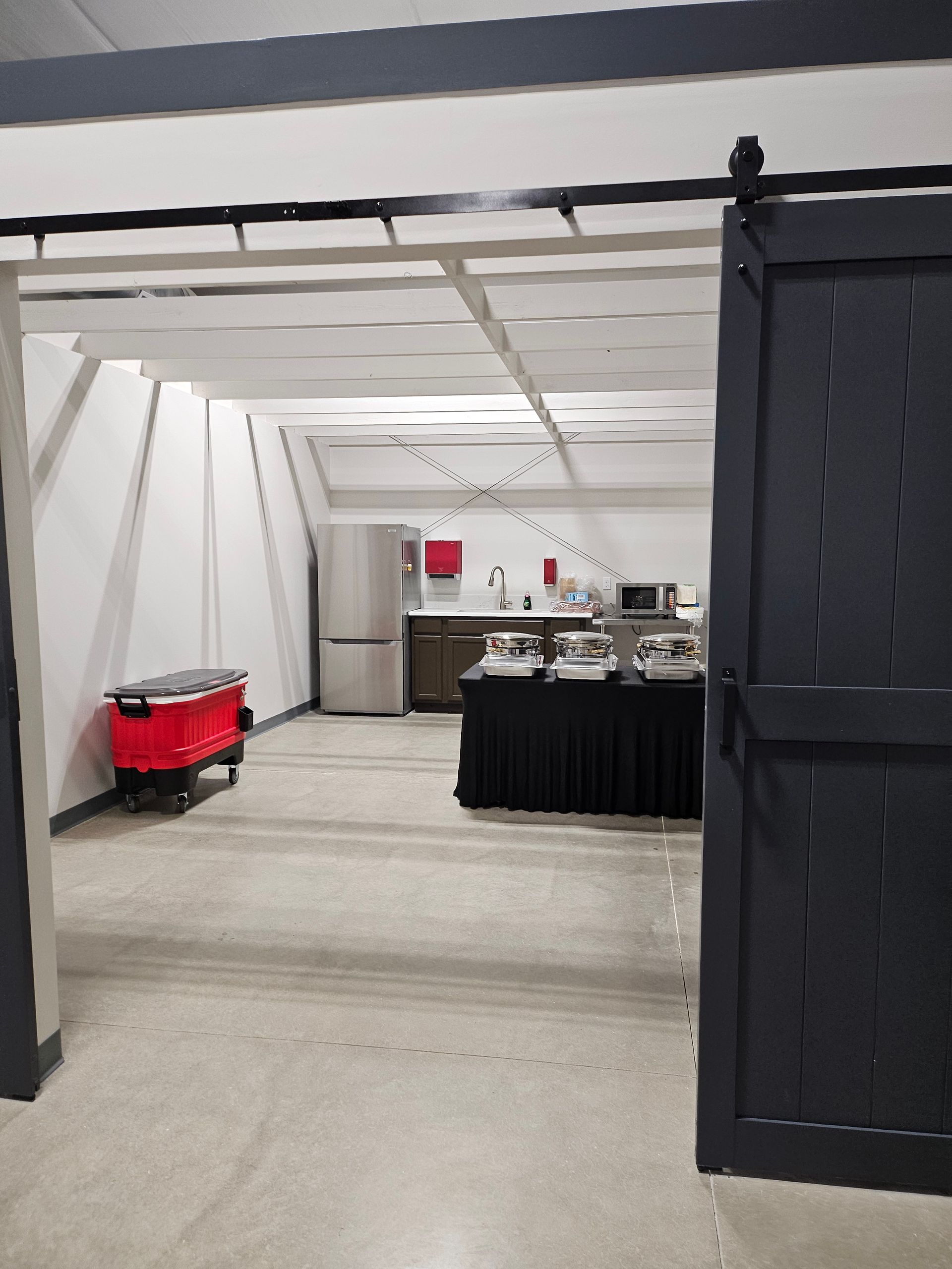 White tented event space with black drapes, a red cooler cart, and buffet tables in the back