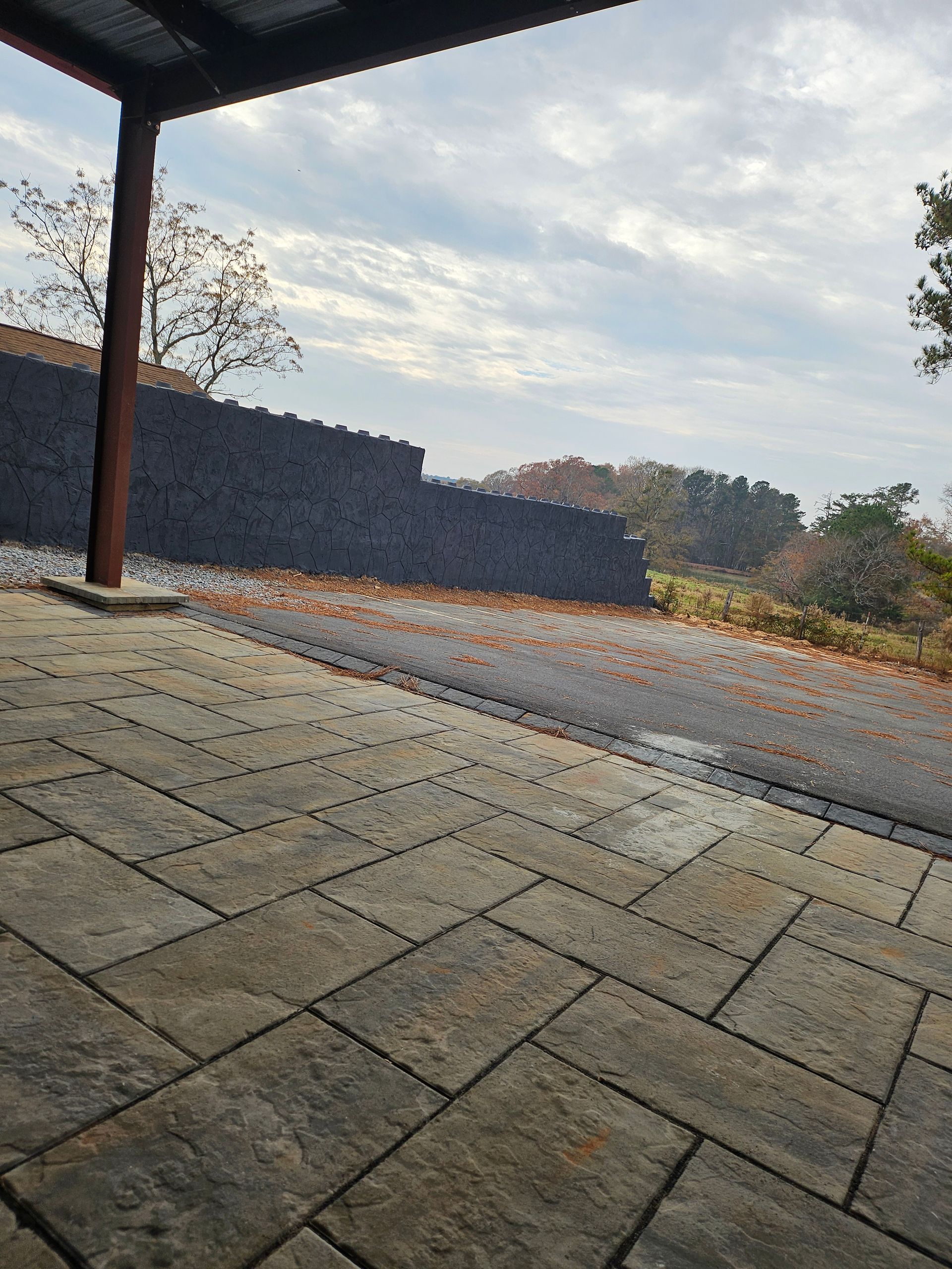 Stone patio under a roof, overlooking a sloped stone wall and cloudy sky at dawn