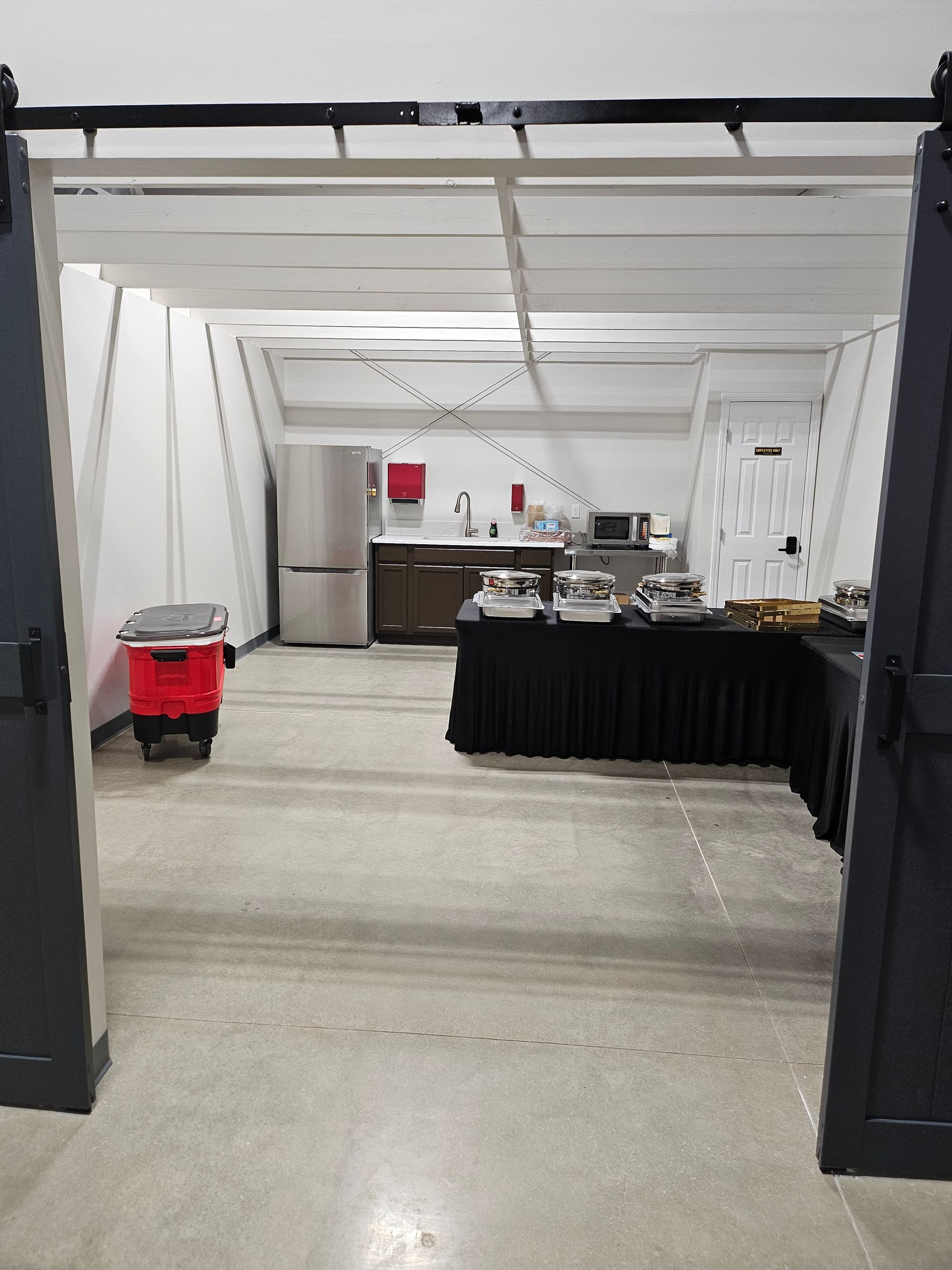 Indoor event room with black-draped buffet tables, stainless kitchen area, and a red mop bucket on the floor