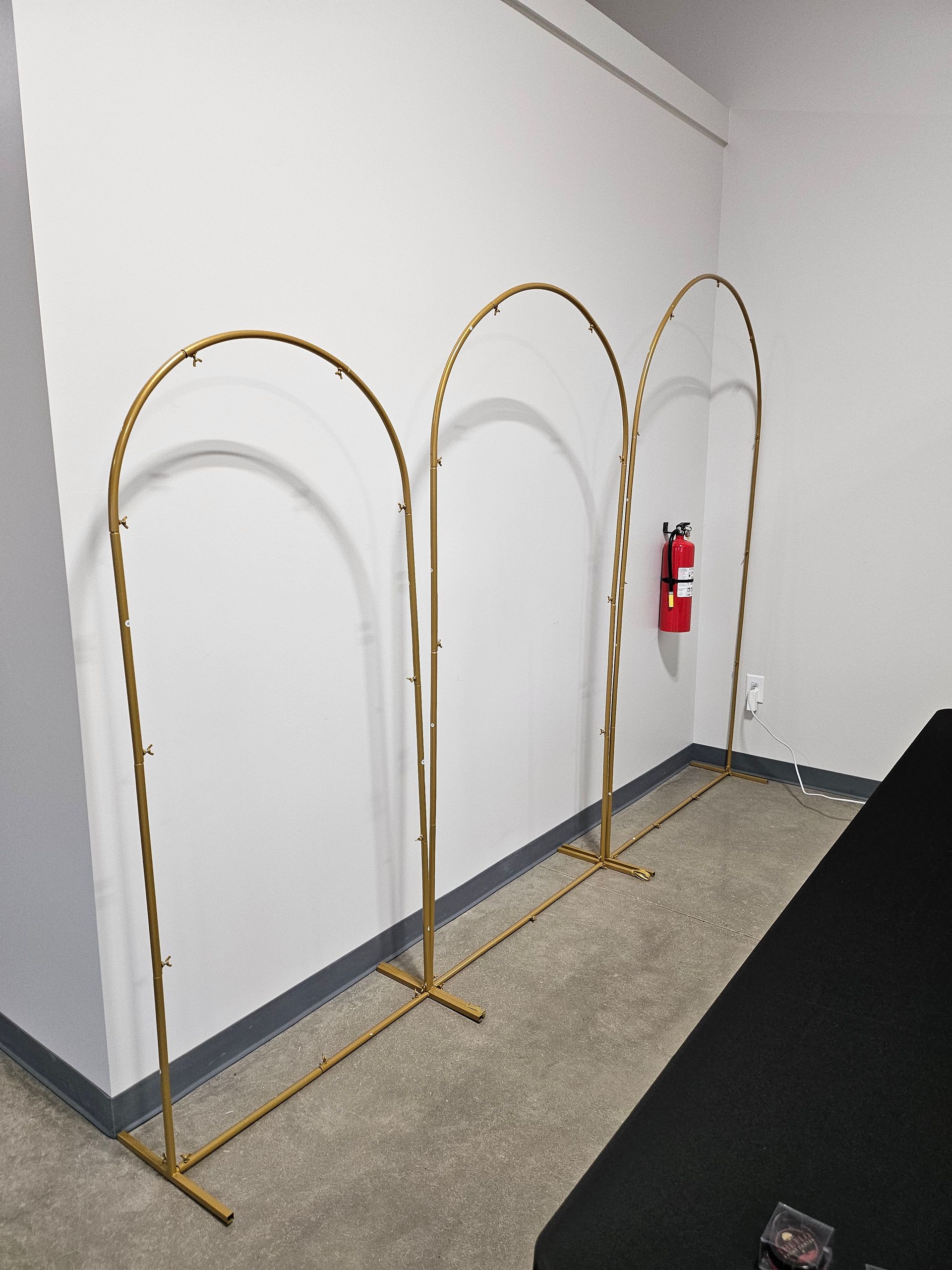 Three gold metal arch frames along a wall beside a red fire extinguisher on a carpeted floor