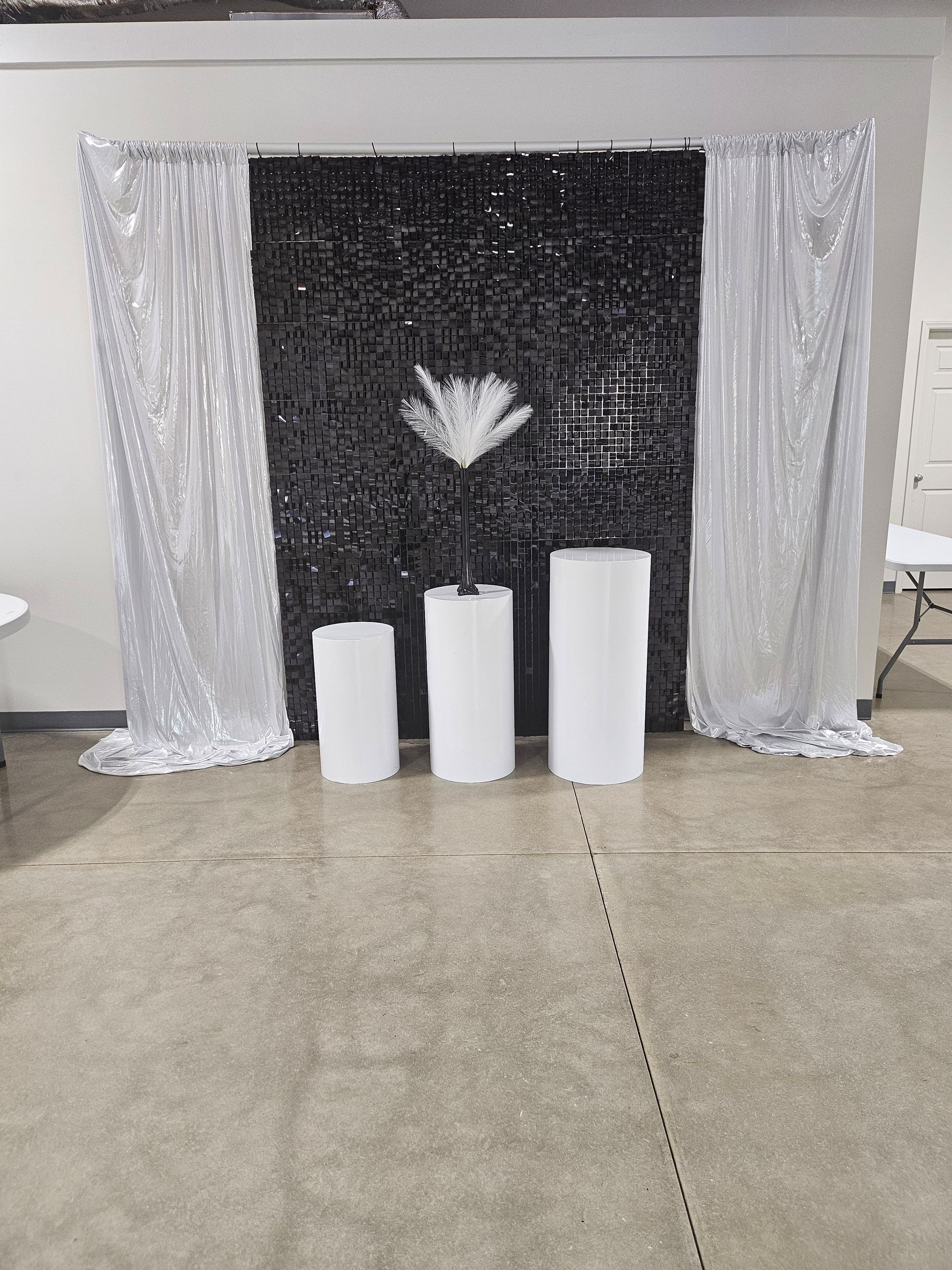 Silver curtains framing a black backdrop with white pedestal columns and a white flower centerpiece on a floor