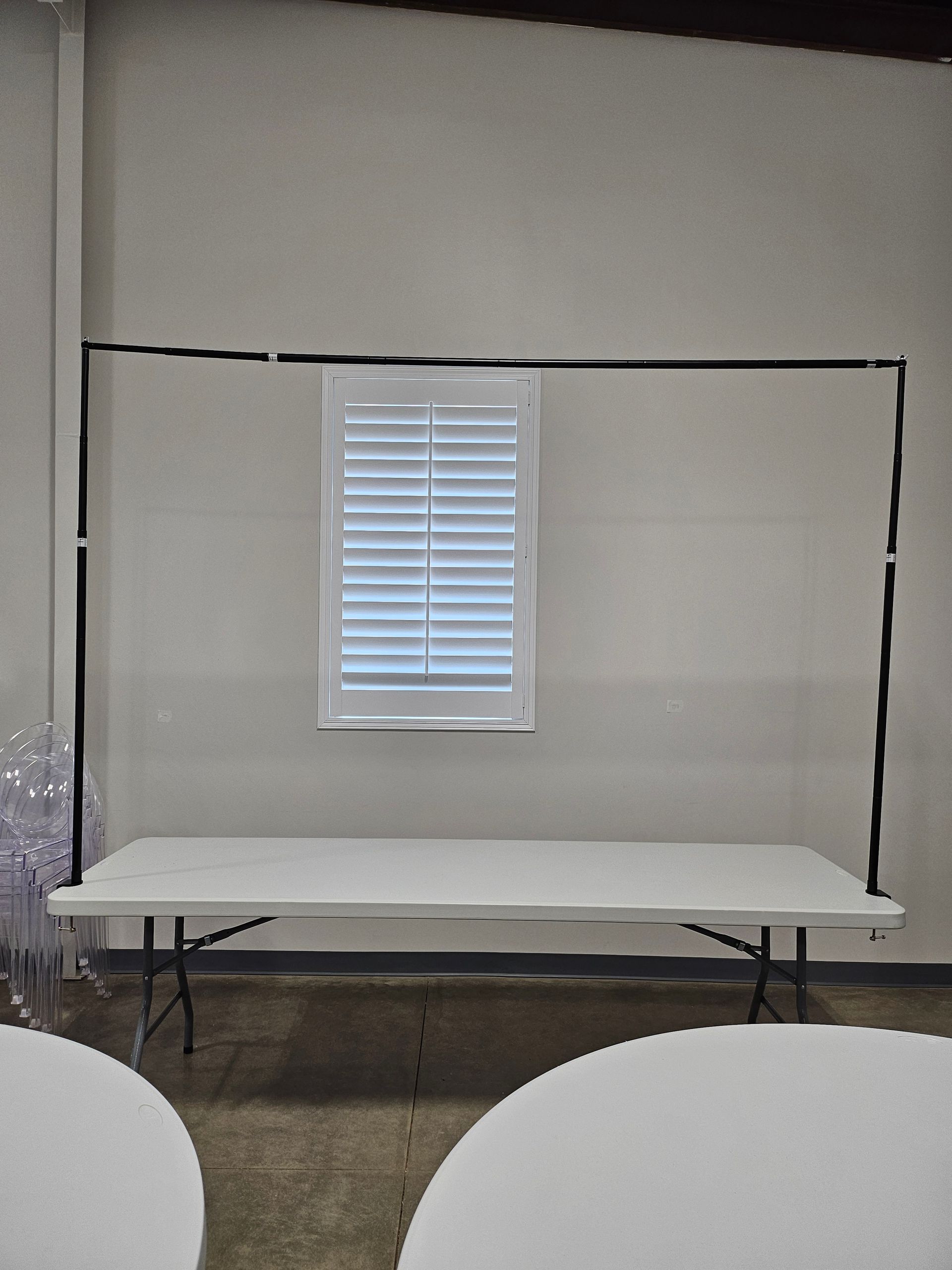 Empty event room with a folding table and a small window with blinds on a blank wall.