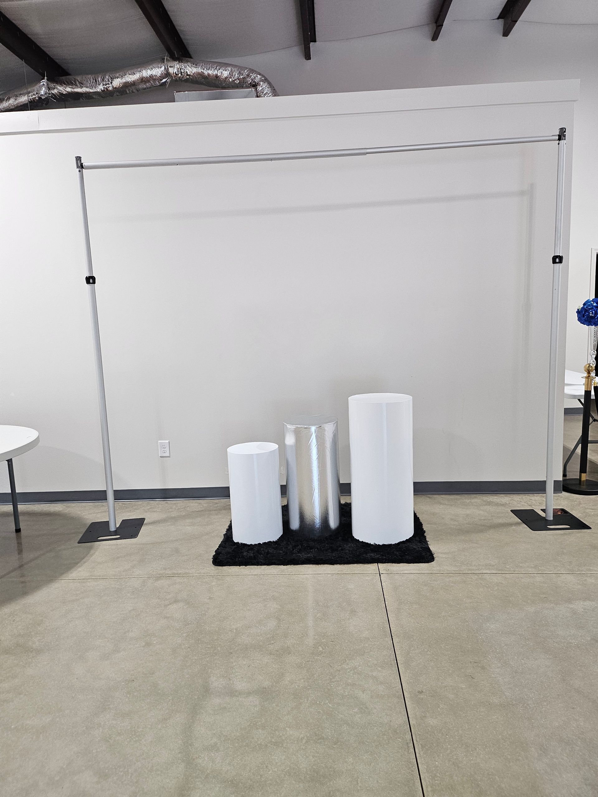 Empty studio backdrop with white wall, black stands, and rolled paper on a rug