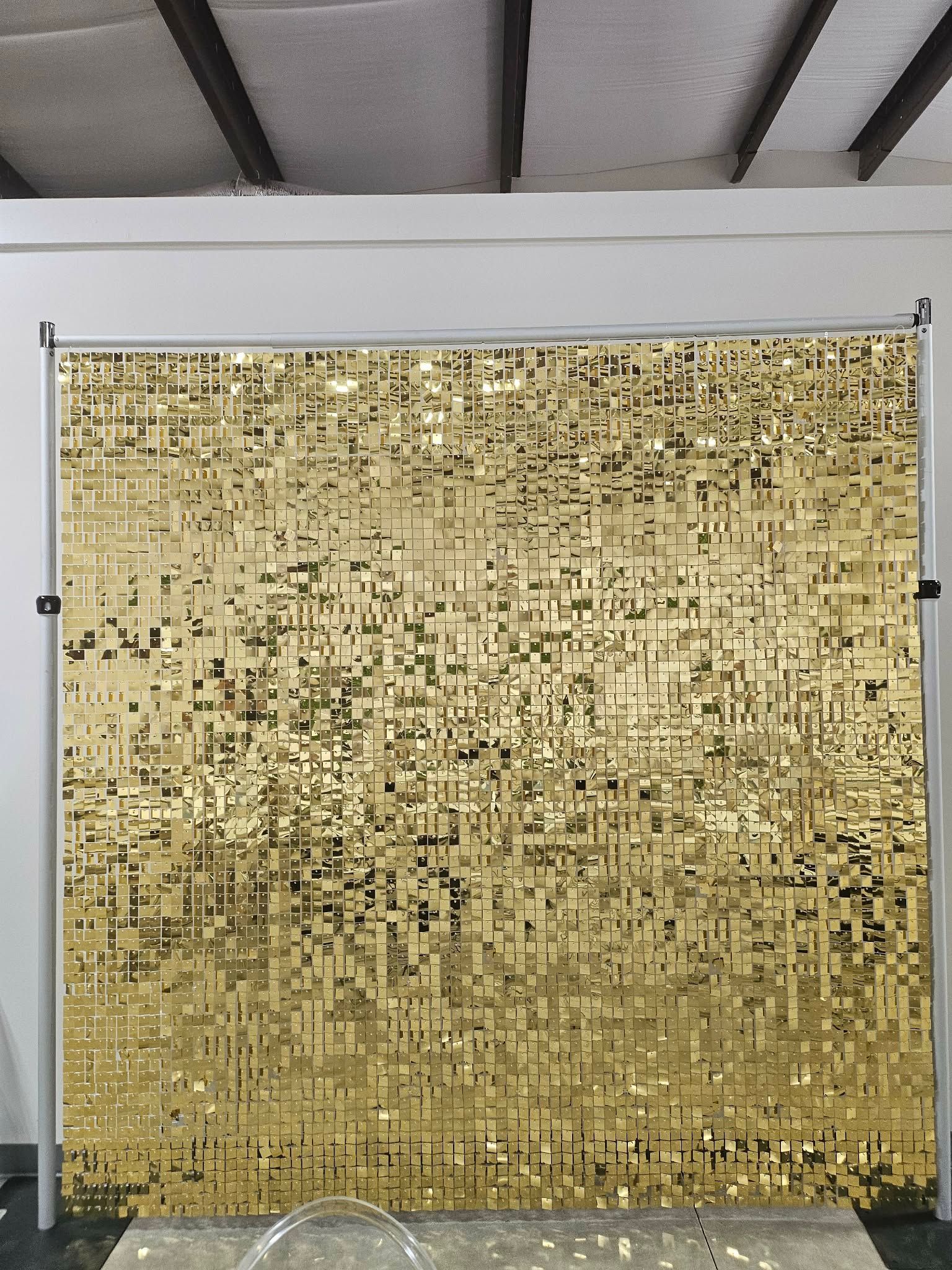 Gold sequin backdrop hanging in an indoor studio with a white wall and ceiling beams.
