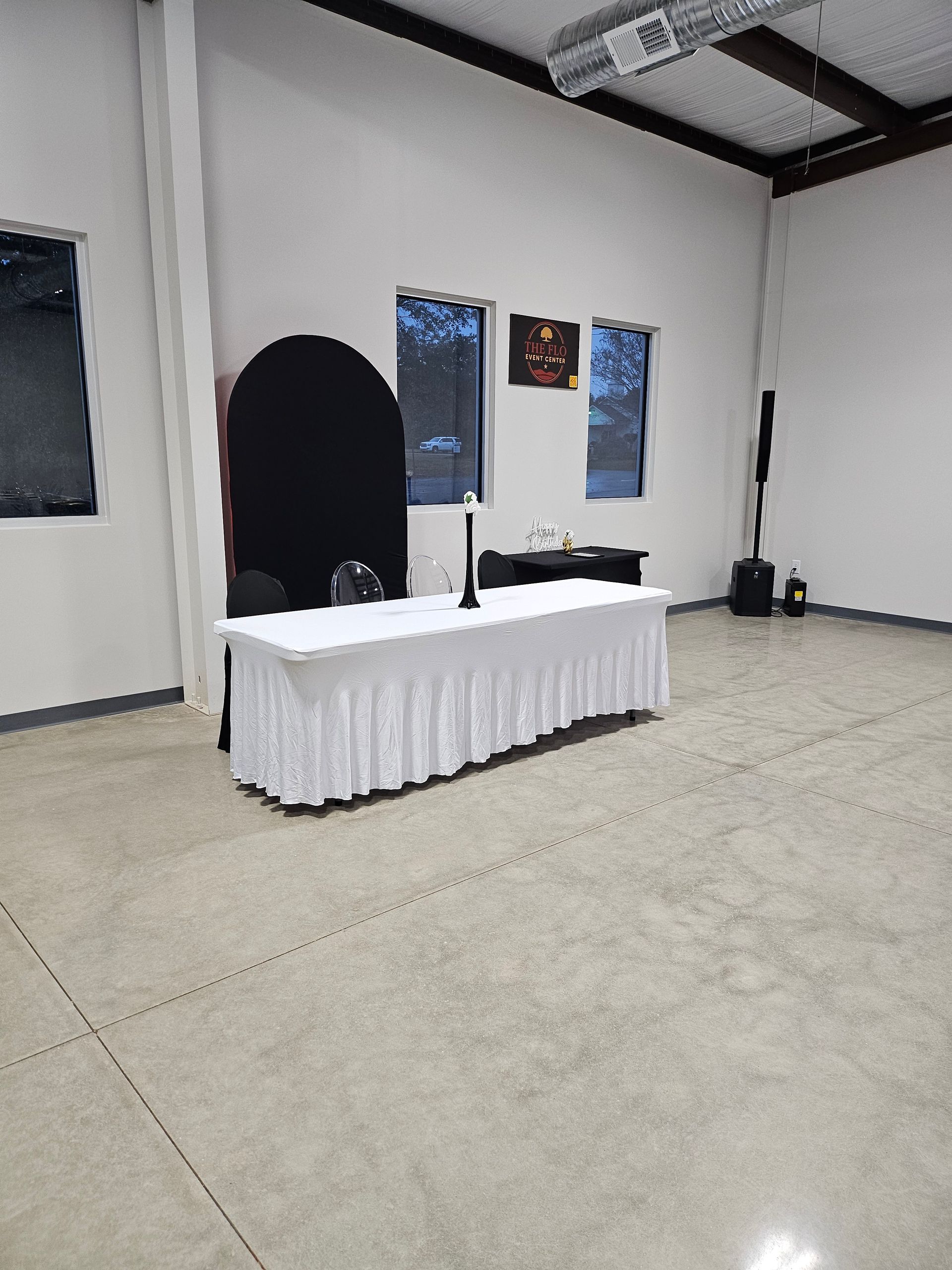 Empty event room with a white-draped table, black backdrop, and posters on the wall.