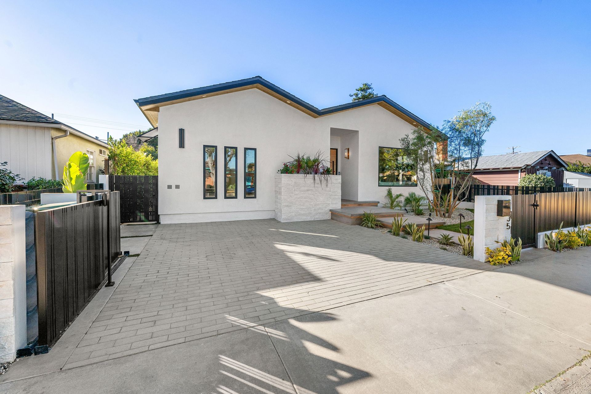 Modern single-story white house with a paved driveway and front garden in bright sunlight
