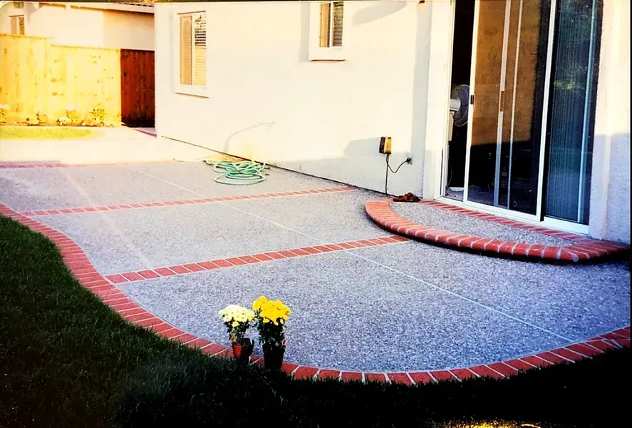 Backyard patio with red-edged gray concrete, sliding glass door, and a small yellow flower pot