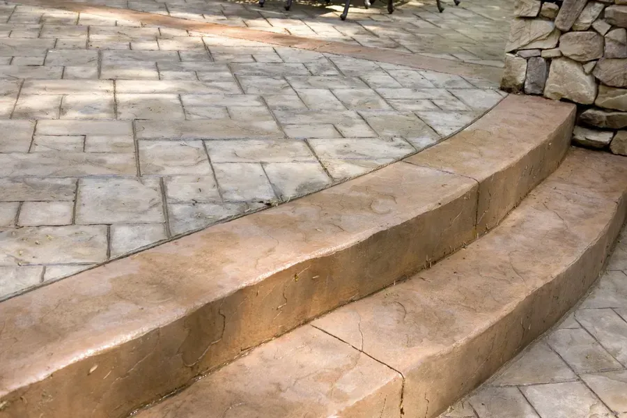 Curved stone steps beside a paved patio and stacked stone wall