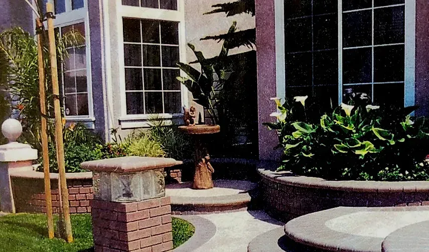Front porch with potted plants, brick columns, and curved white benches by a house entrance.