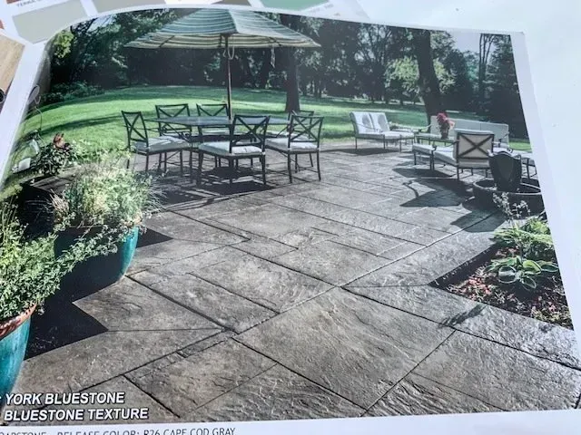 Stone patio with black metal outdoor dining furniture, potted plants, and a lawn beyond