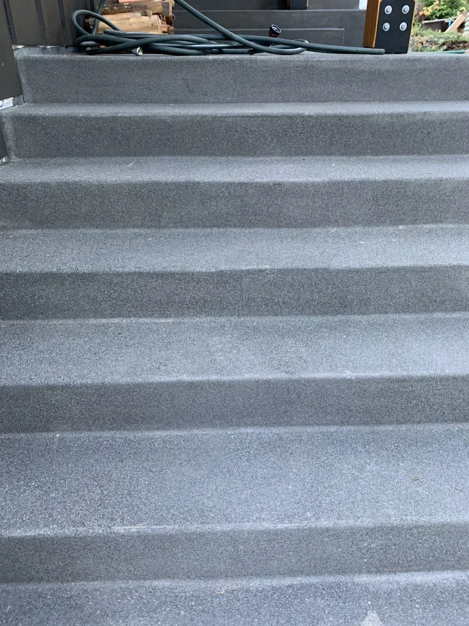 Gray carpeted stairs leading upward indoors, with a small piece of furniture at the top left.