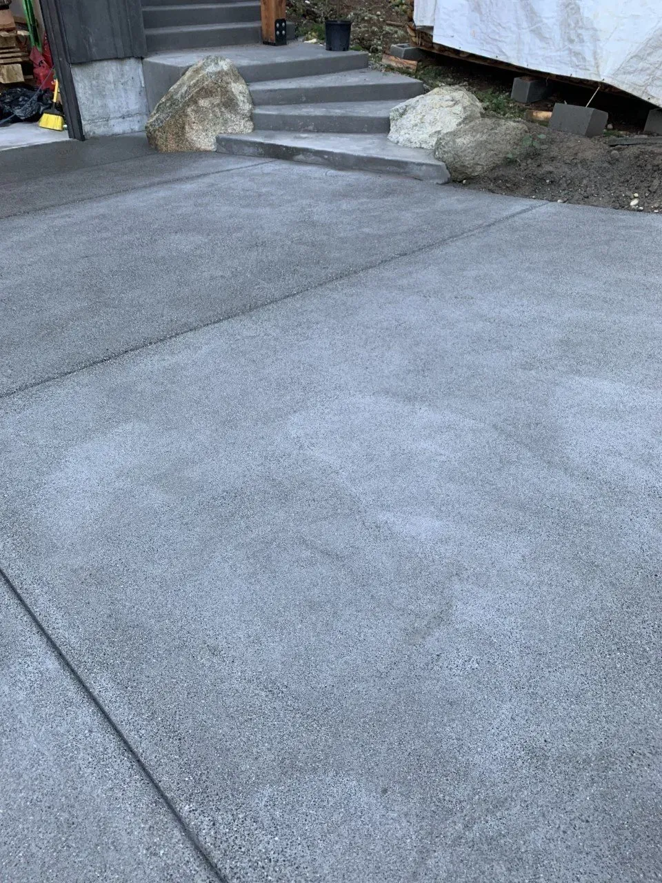 Large gray paved driveway with stone steps and rocks beside a house