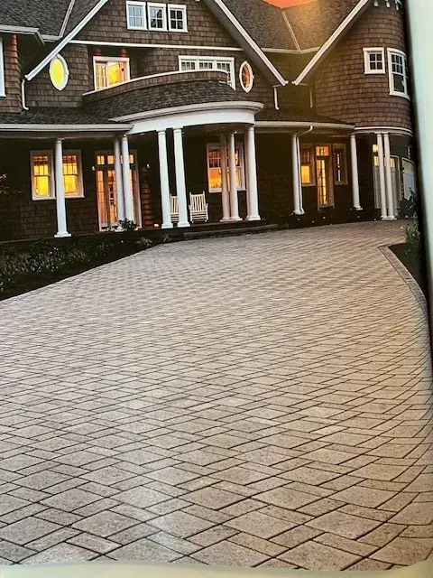 Brick courtyard leading to a brick building with white columns and lit windows at dusk