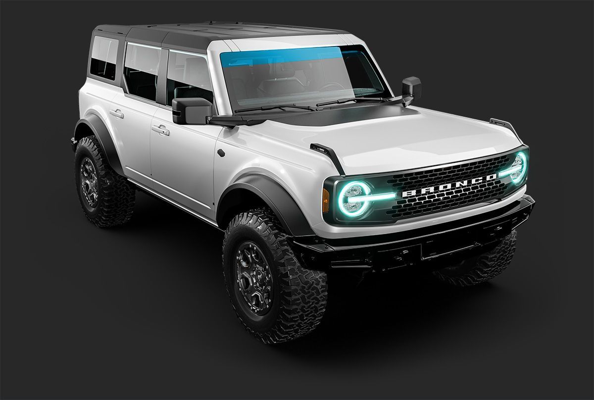 A white four-door Ford Bronco SUV with large black tires and glowing circular LED headlights against a dark background.
