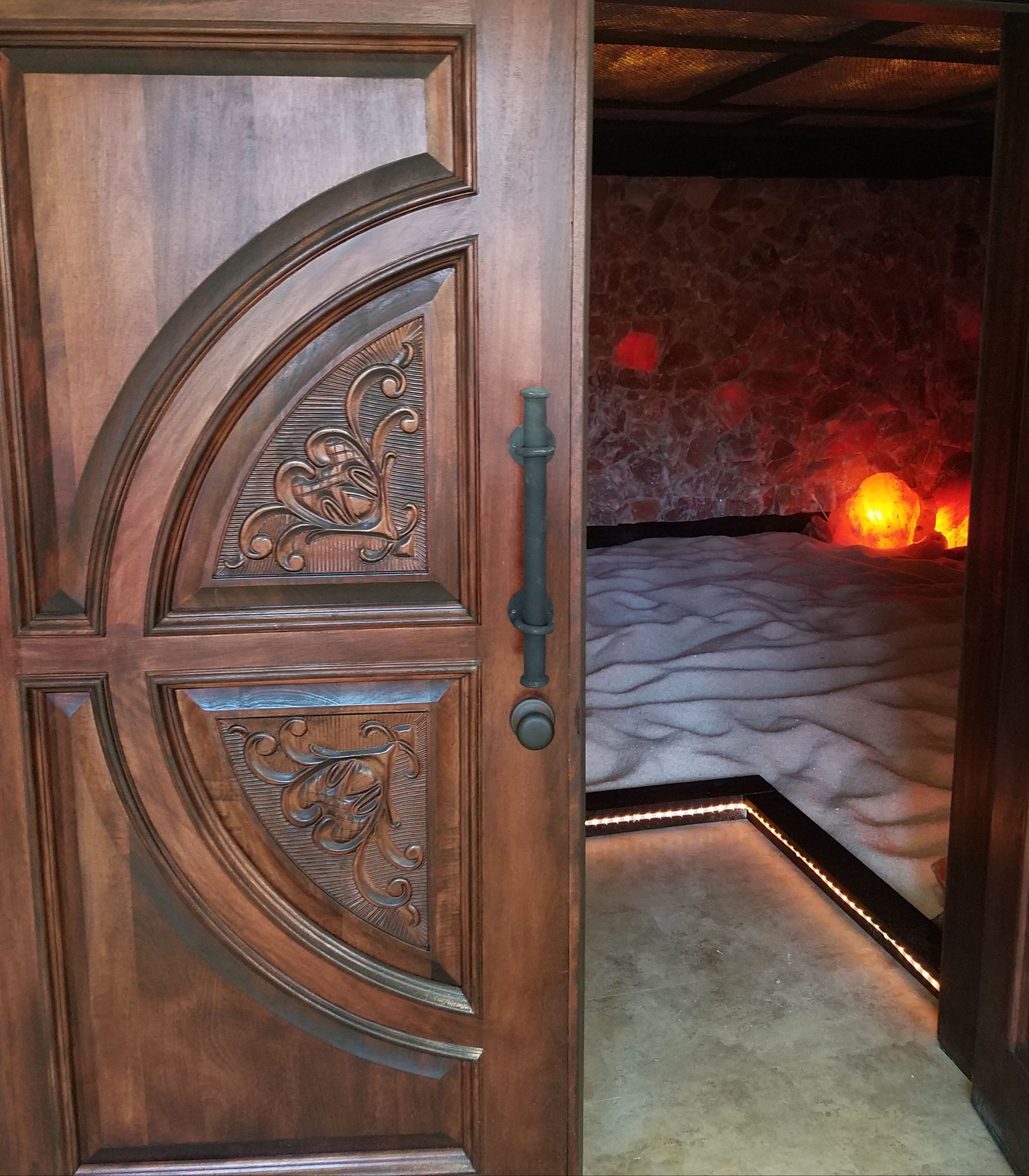 Wooden door with carved details partially open to reveal a salt cave with glowing lights.